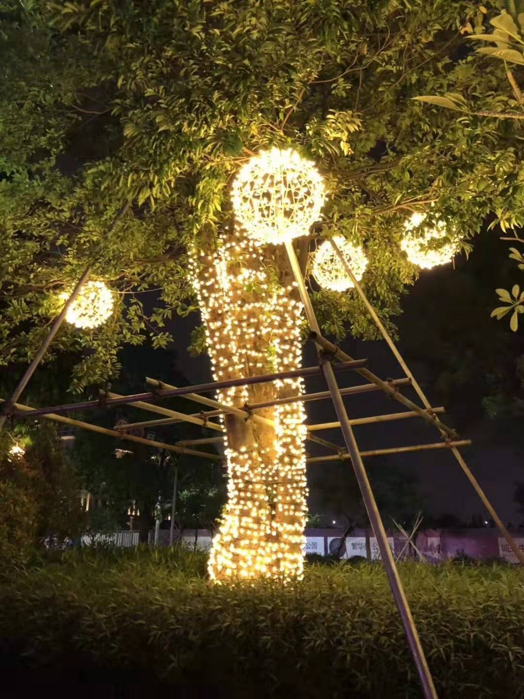 中山市瀚沃灯饰有限公司授权档案:档案环境外观参考:多个带亮点的镂空球状对象悬在树冠附近,树干另有绕线;悬挂结构、材质及项目归属未核实。